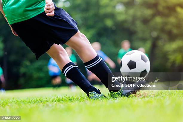 primer plano de niño pateando pelota de fútbol durante el juego - shinguard fotografías e imágenes de stock