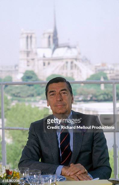 Claude Terrail sits at a dining table in his famous establishment. The Cathedral of Notre Dame de Paris can be seen through the window behind him.