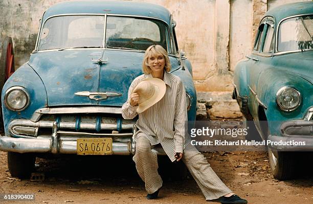 French actress Mireille Darc seated on the fender of an old Chevrolet on the set of the 1996 mini series Terre Indigo.