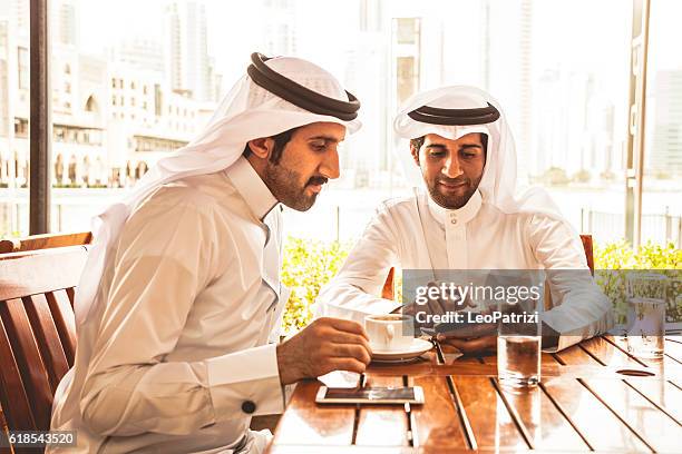 talking about business at a cafe in dubai - emirati laptop stock pictures, royalty-free photos & images