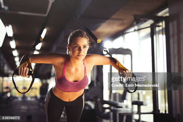 woman doing arm exercises with suspension straps at gym. - suspension training stockfoto's en -beelden