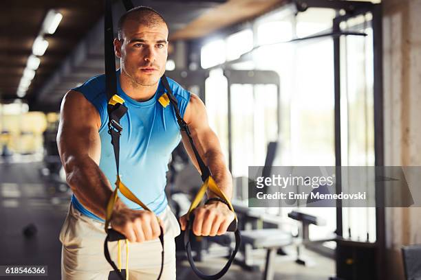 man doing arm exercises with suspension straps at gym. - suspension training stockfoto's en -beelden