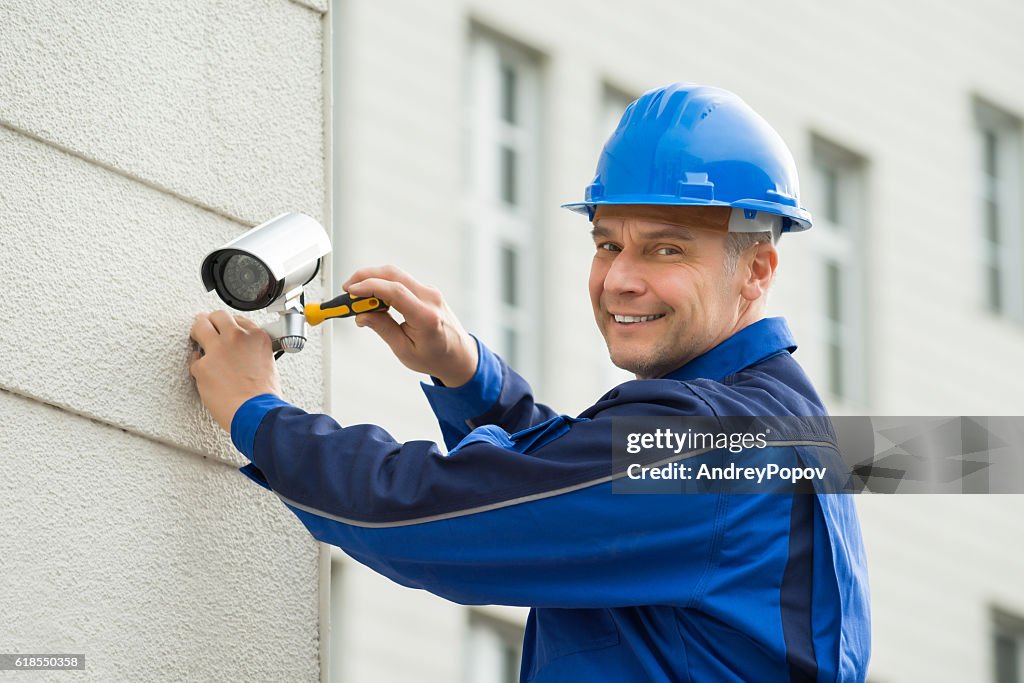 Mature Technician Installing Camera On Wall With Screwdriver