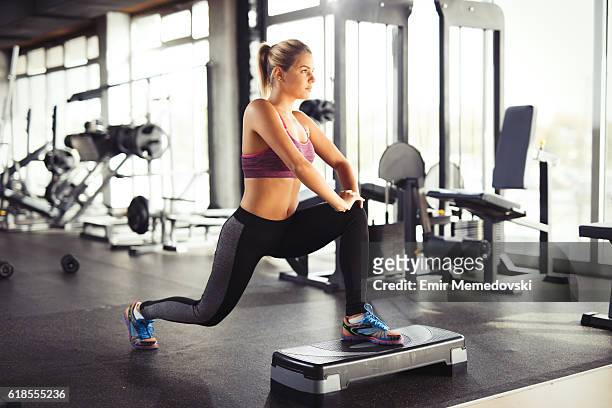 young woman doing lunges on step aerobics equipment at gym. - lunge imagens e fotografias de stock