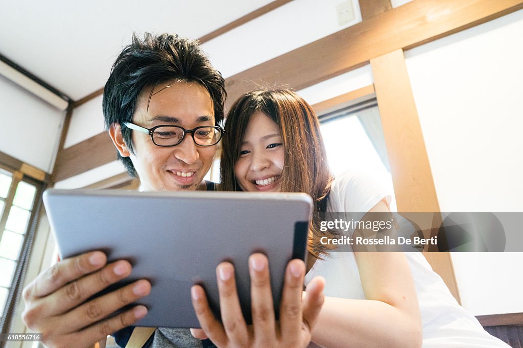 Cheerful Japanese friends using tablet indoors