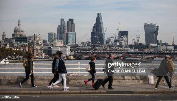 Pedestrians walking through Waterloo Bridge with the skyline of the City of London in the background on October 27, 2016. - Britain's economy won a...