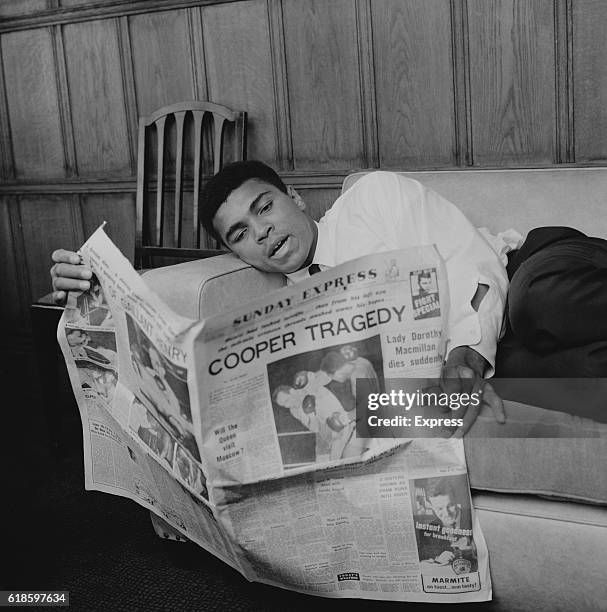 American boxer Muhammad Ali reading the Sunday Express newspaper in his hotel room, London, UK, 22nd May 1966. The headline 'Cooper Tragedy' refers...