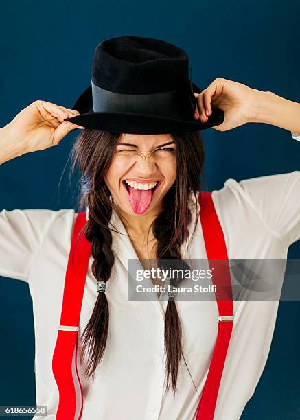 beautiful brunette with two braids smiles at the camera with tongue out - women in suspenders fotografías e imágenes de stock