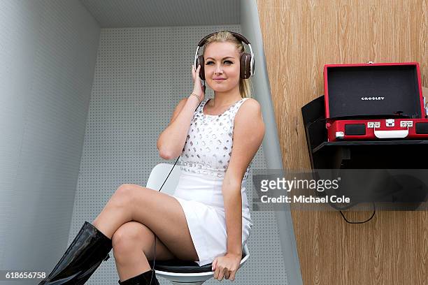 Girl in 60s dress wearing headphones, sitting in the Listening Booth Installation themed around the 1960s record shops at Goodwood on September 9,...