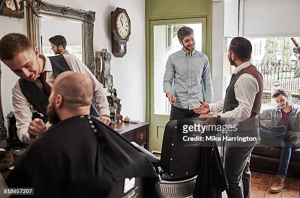 male barber inviting customer to take a seat - busy barber shop stock pictures, royalty-free photos & images