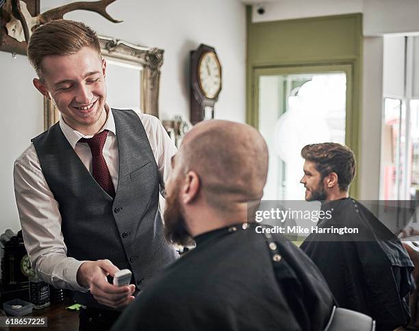 young male barber giving a beard trim - busy barber shop stock pictures, royalty-free photos & images