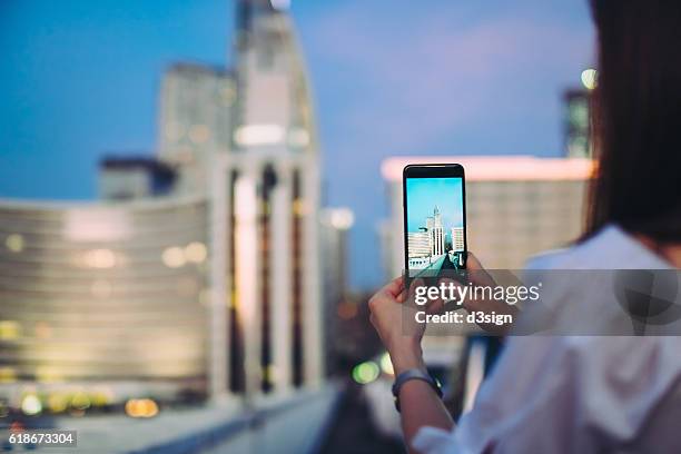 woman using smartphone to capture city scene at night - woman capturing city night foto e immagini stock