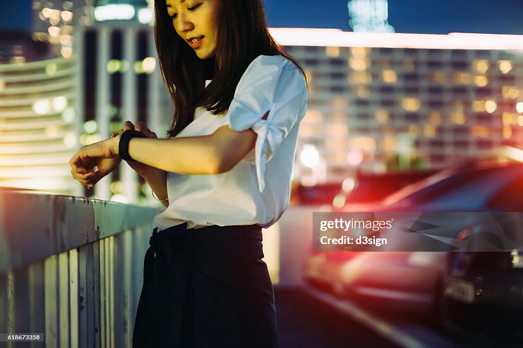 Young Asian businesswoman checking her smart watch in the city at night