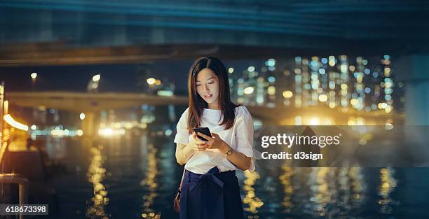 young asian girl using smartphone in front of the hong kong city skyline at night - urban areas　water front stockfoto's en -beelden