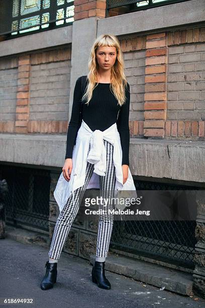 Model Nova Orchid wears a black sweater, a white jacket tied around her waist, a black houndstooth print pants, and black booties after the Lemaire...