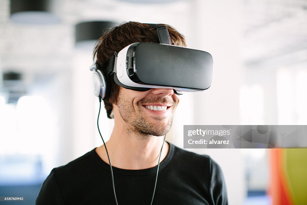Uomo d'affari sorridente che usa il simulatore VR in ufficio