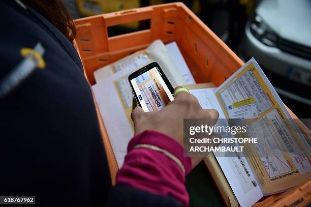 Postwoman Celia Ruivo-Alves scans a bar code on an envelope during her morning round in Chevilly-Larue, southern Paris, on October 20, 2016. The new...