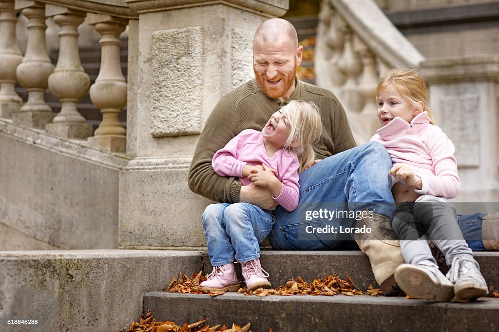 Single father and daughters laughing together on stately autumnal steps