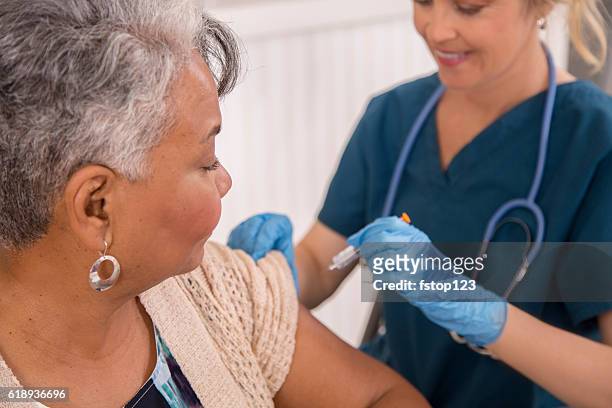 nurse gives flu vaccine to senior adult patient at clinic. - flu vaccination stock pictures, royalty-free photos & images