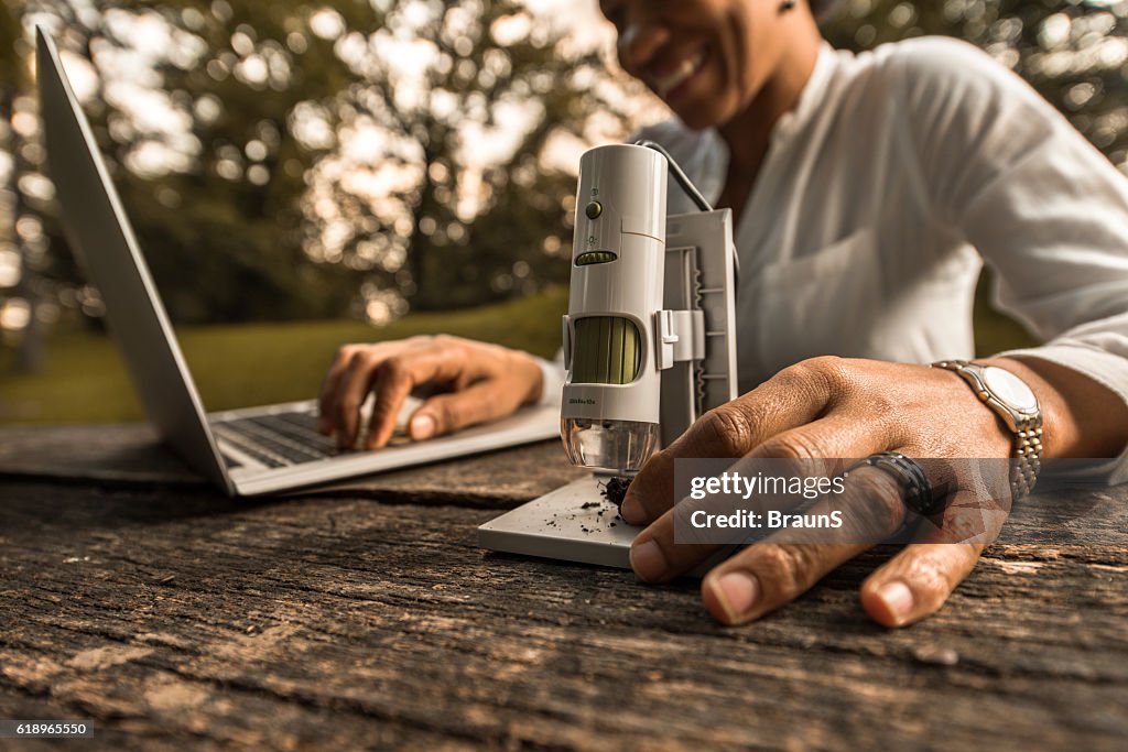 Close up of businesswoman working with microscope and laptop outdoors.