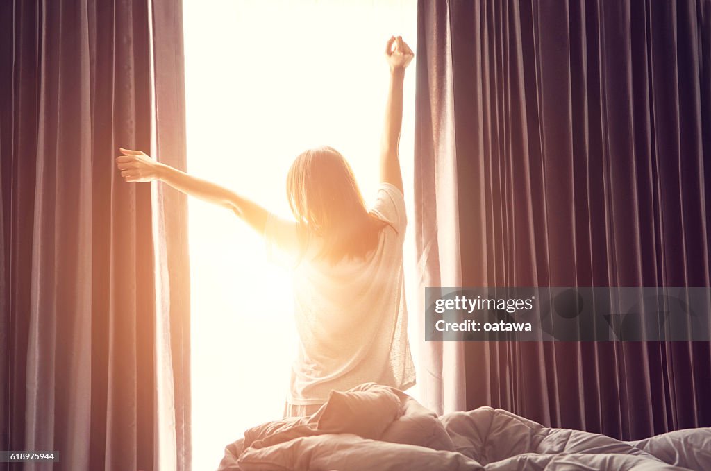 Mulher se alongando perto da cama depois de acordar