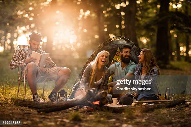 gruppo di amici felici seduti accanto al falò e che si divertono. - four people smiling foto e immagini stock