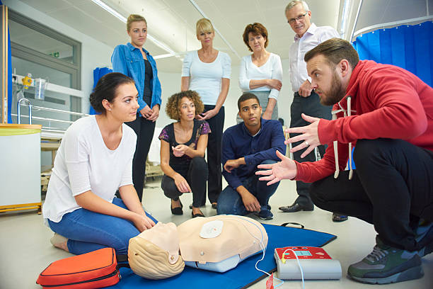 Man in front of a dummy, teaching a group of people how to give CPR.