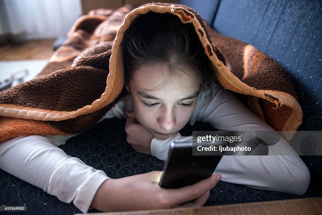 Female teen using phone in bed during the day