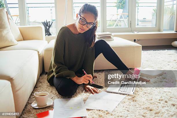 junge frau studiert in ihrem wohnzimmer - geld und finanzen stock-fotos und bilder