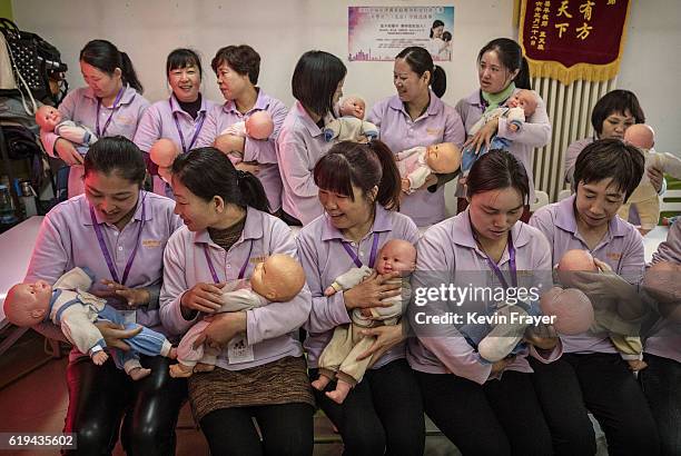 Chinese women hold plastic babies as they prepare for a class photo at a course to train to be qualified nannies, known in China as ayis, at the Ayi...