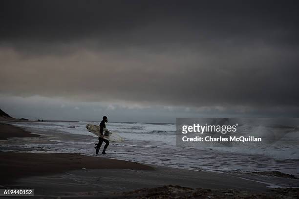 Professional surfer Al Mennie makes his way along Whiterocks beach to catch a wave under the historic Dunluce Castle ruins on October 31, 2016 in...