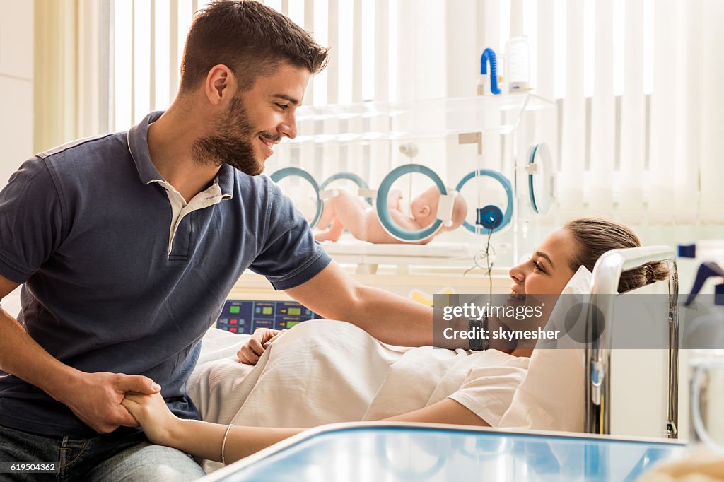 Smiling new parents looking at each other in hospital nursery.