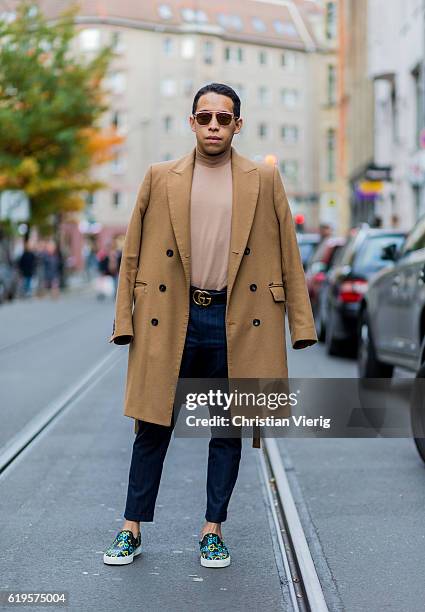 Eduardo Cano wears a beige wool coat, beige turtleneck sweater, sunglasses, Gucci belt, navy stripped pants, Gucci loafers, Gucci slipper loafers on...