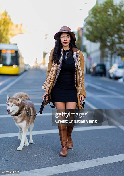 Lucia Amelia Pimentel with her husky dog wears a Louis Vuitton scarf, brown hat, beige wool coat, plaid jacket, black dress, socks and brown boots on...