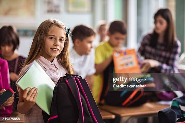 smiling schoolgirl in the classroom packing her books into backpack. - packing kids backpack stockfoto's en -beelden