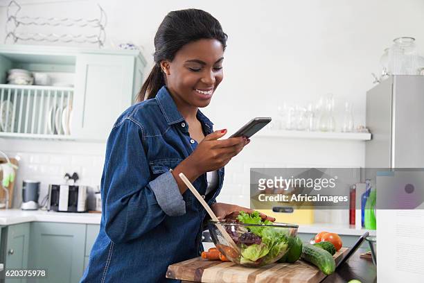mujer africana riéndose de un mensaje de texto en su teléfono celular. - meal plan fotografías e imágenes de stock