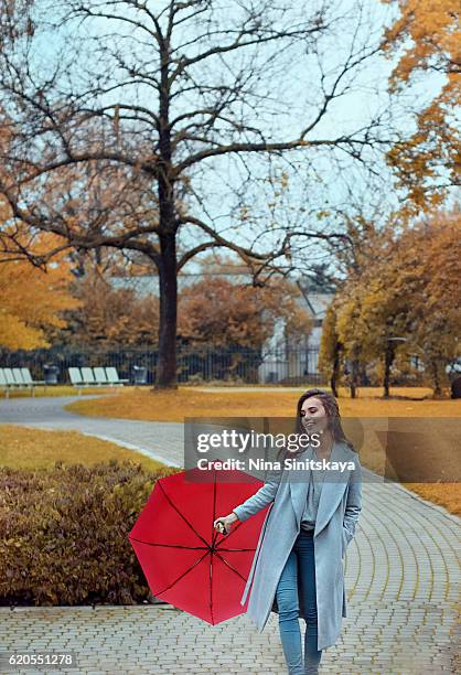 happy looking woman in grey coat with red umbrella walking in the park - warsaw stock pictures, royalty-free photos & images