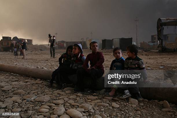 Children look on as fire fighters try to extinguish the fire at oil wells, were set on fire by Daesh terrorists as they fled after Al Qayyarah town's...