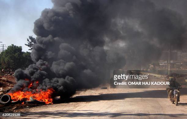 Rebel fighters from the Jaish al-Fatah brigades drive past burning tyres on November 3 at an entrance to Aleppo, in the southwestern frontline near...