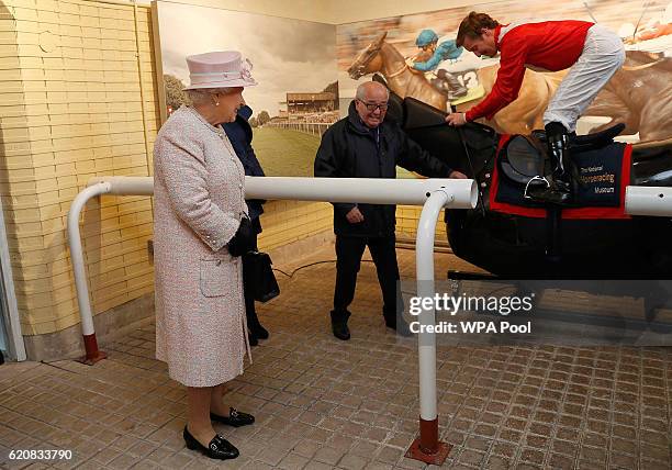 Queen Elizabeth II watches jockey Pat Cosgrove on a simulator during a visit to the National Heritage Centre for Horseracing and Sporting Art on...