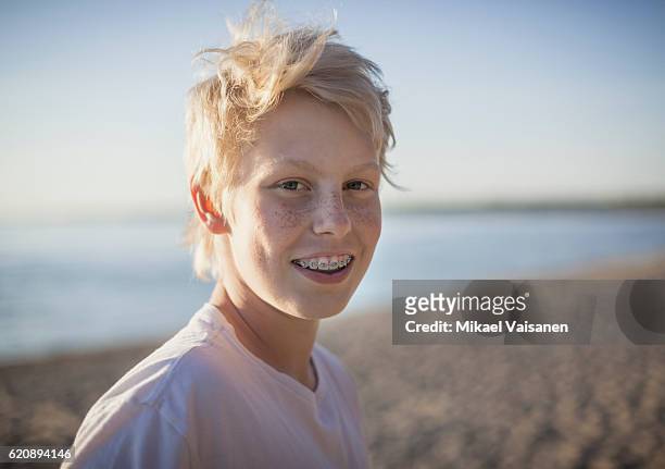 portrait of teenage boy with braces on the beach - season 15 stock-fotos und bilder