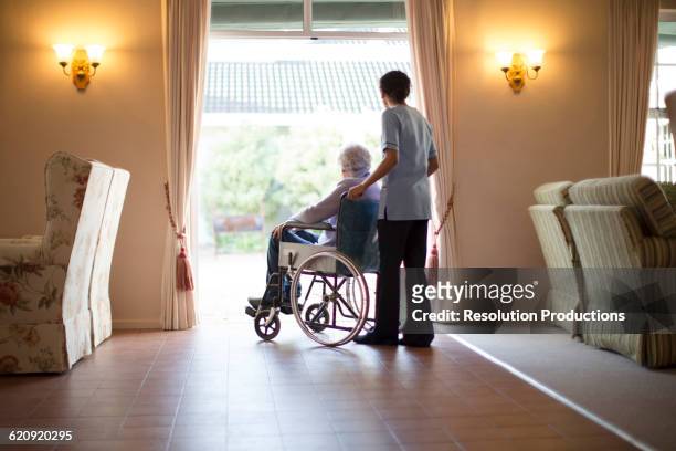 nurse pushing patient in wheelchair - rentnersiedlung stock-fotos und bilder