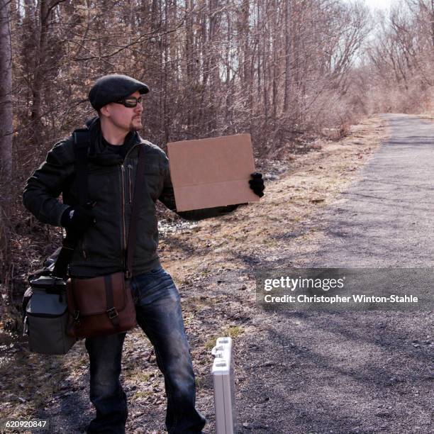 man hitchhiking with blank sign on rural road - christopher hitch fotografías e imágenes de stock