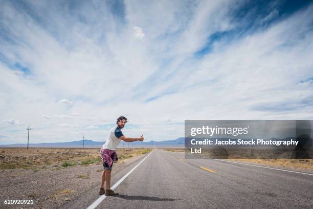 hispanic man hitchhiking on remote road - trampen stock-fotos und bilder