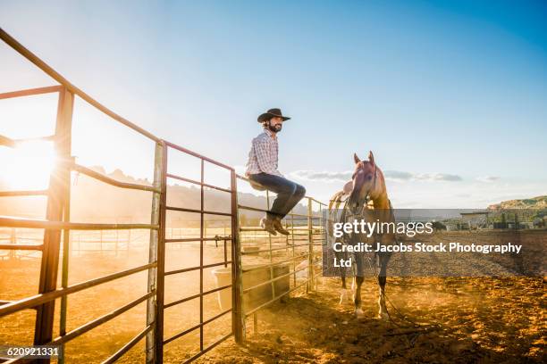 hispanic man sitting on fence near horse - rancho fotografías e imágenes de stock