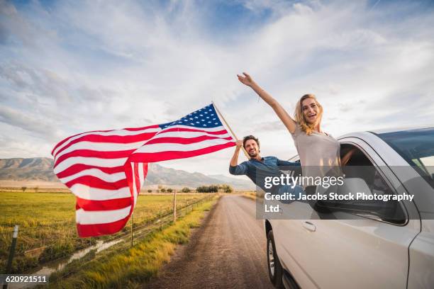 hispanic couple waving american flag out car window - independence day holiday stock pictures, royalty-free photos & images