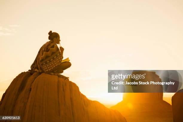 hispanic woman sitting on rock formation in remote desert - roman landscapes stockfoto's en -beelden