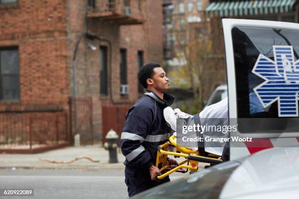 mixed race paramedic loading patient into ambulance - stretcher stock-fotos und bilder