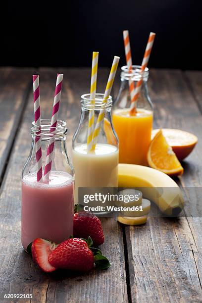 row of three bottles with different fruit smoothies and orange juice - batido de fresa fotografías e imágenes de stock