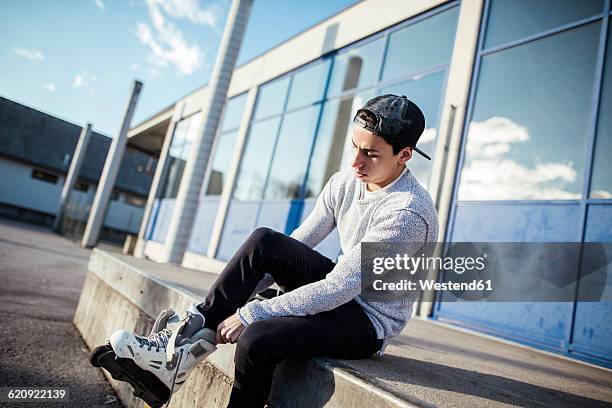 young man sitting on ramp putting on inline skates - inline skating - fotografias e filmes do acervo